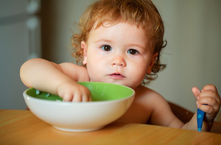 portrait funny little baby boy eating from plate holding spoon closeup scaled